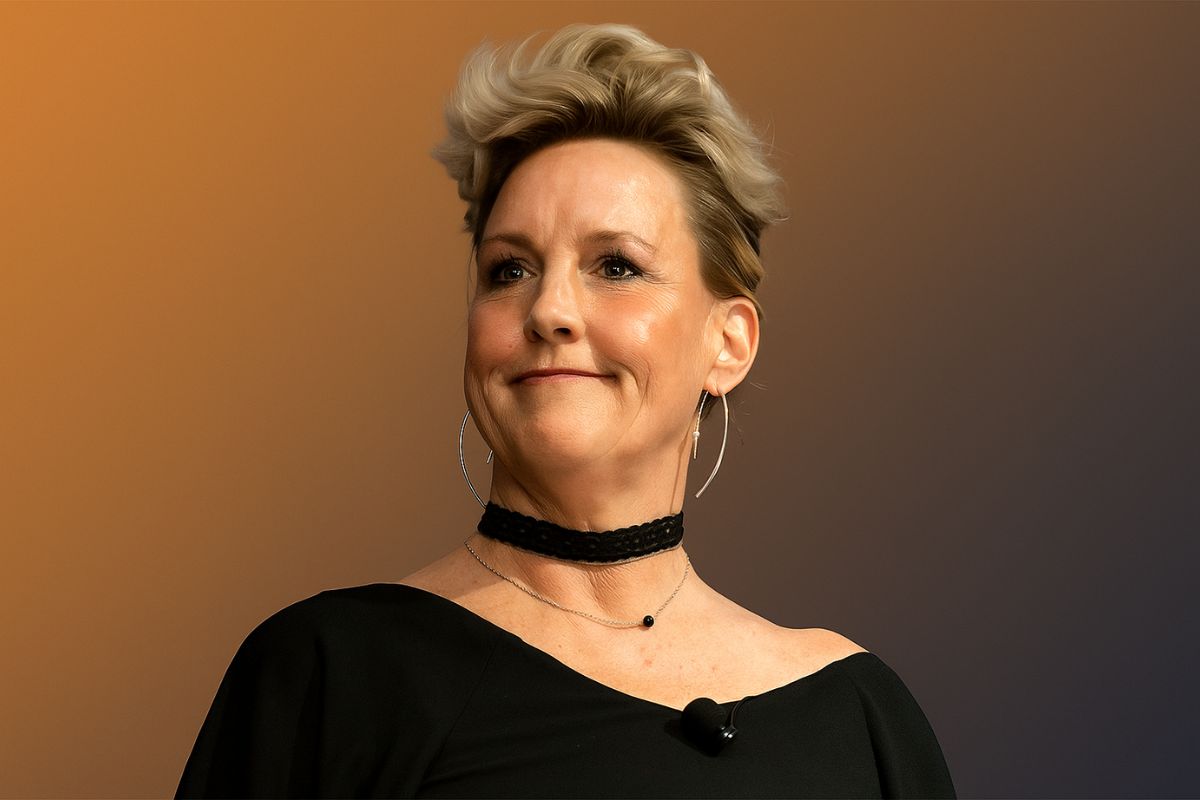 an image of erin brockovich in black outfit wearing a black neck band and brown-black gradient background representing net worth of erin brockovich